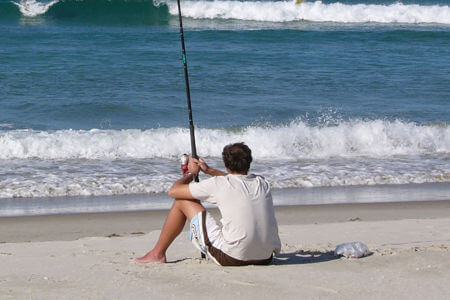 Young man sitting on beach fishing in Buxton, NC.